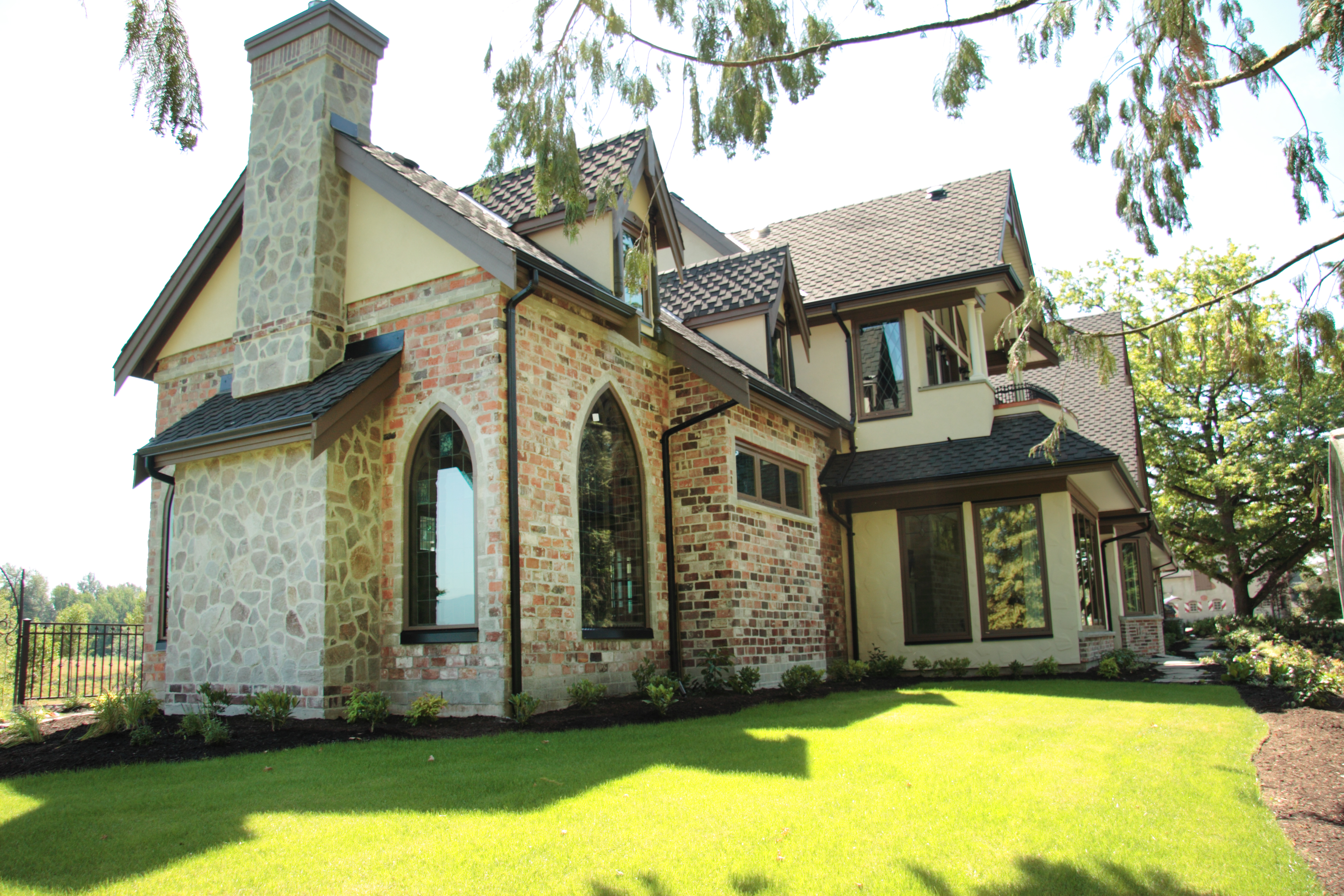 The exterior view of a traditional style home with brick and stucco siding with custom shape vinyl brown windows. 
