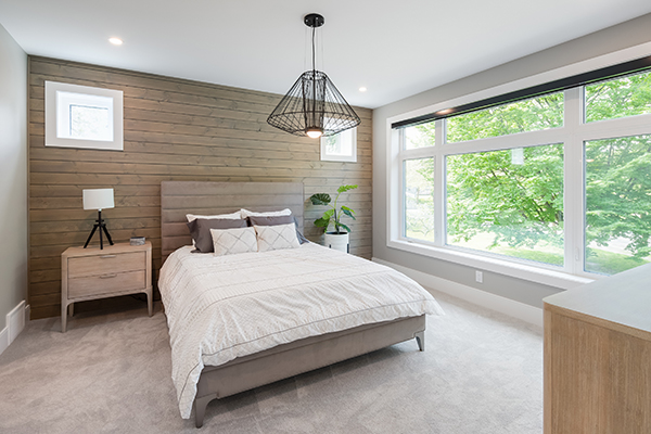 A bright and spacious master bedroom interior with a hanging light fixture and large white modern collection vinyl windows.