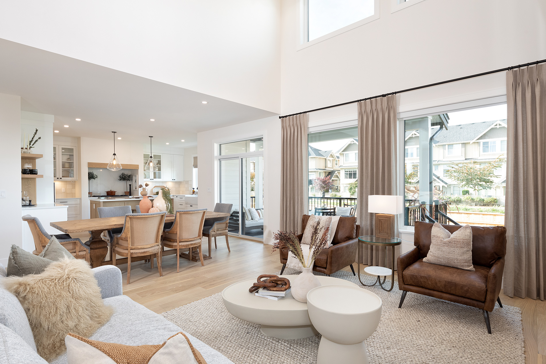 A bright open concept living room interior with large white vinyl windows with hanging brown curtains. 